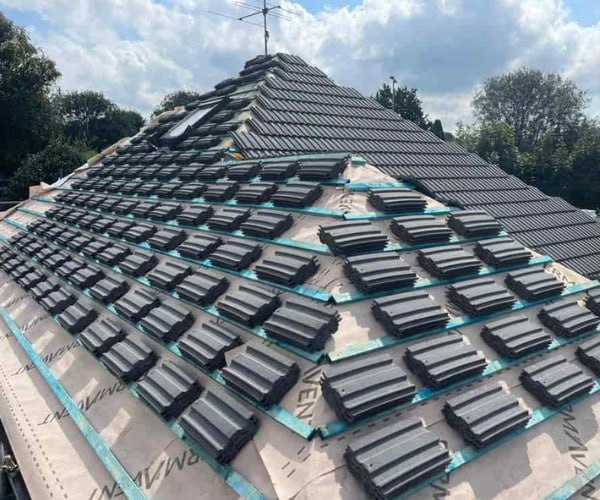 This is a photo of a new hip roof being installed. New felt, battens, and grey tiles have been installed, also a new velux window. Works carried out by SC Roofing Olney