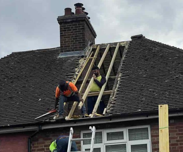 This is a photo of a roof repair being carried out. A section of the roof has been stripped and two roofers are replacing the rafters. Works being carried out by SC Roofing Olney